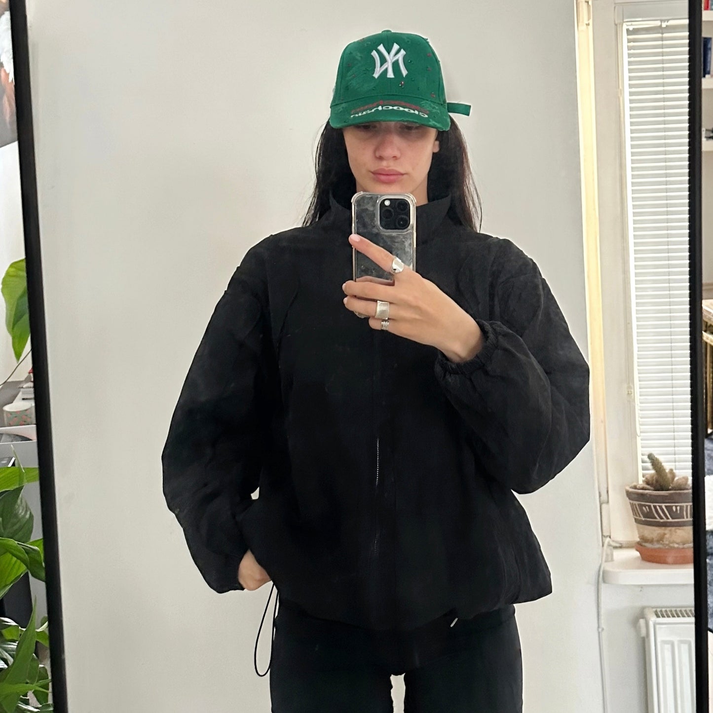 Person wearing a black outfit with a green cap indoors.