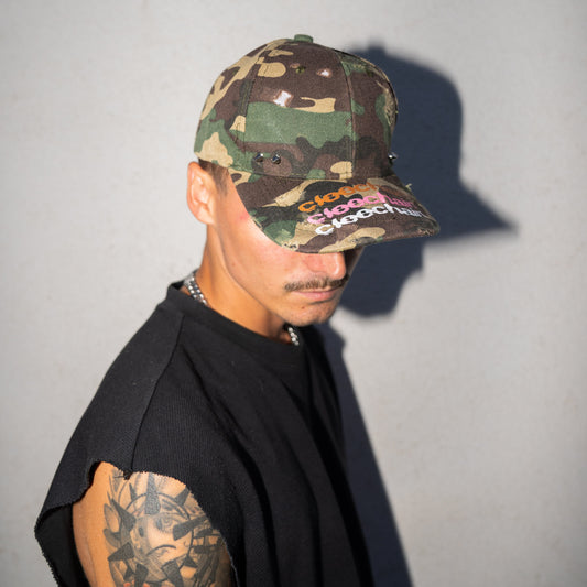 Person wearing a camouflage cap with text, standing against a plain background